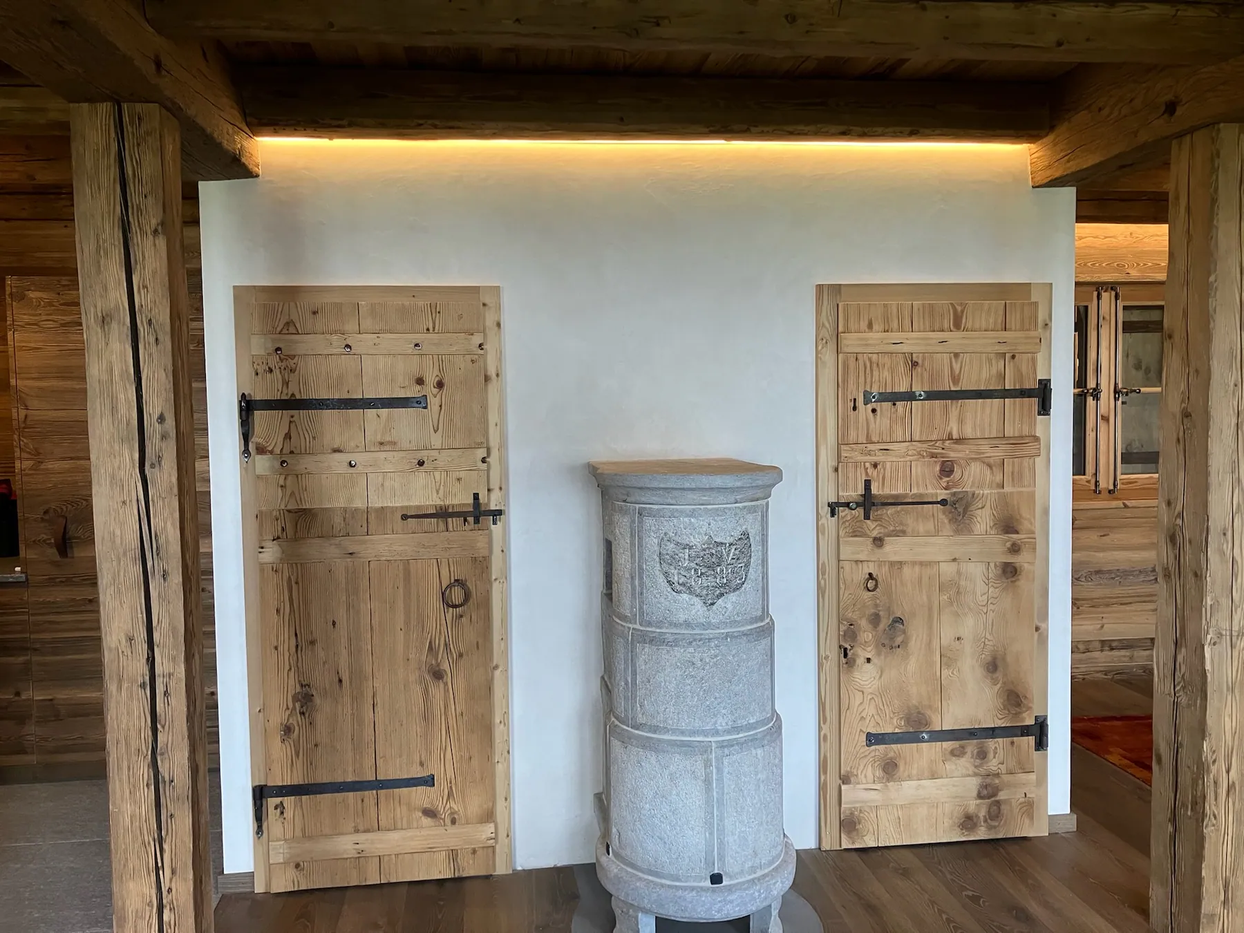 Un couloir chaleureux avec des portes en bois massif et un poêle en pierre au centre, souligné par des poutres apparentes — chantier Bio Rénovation, Villars-Gryon (VD)