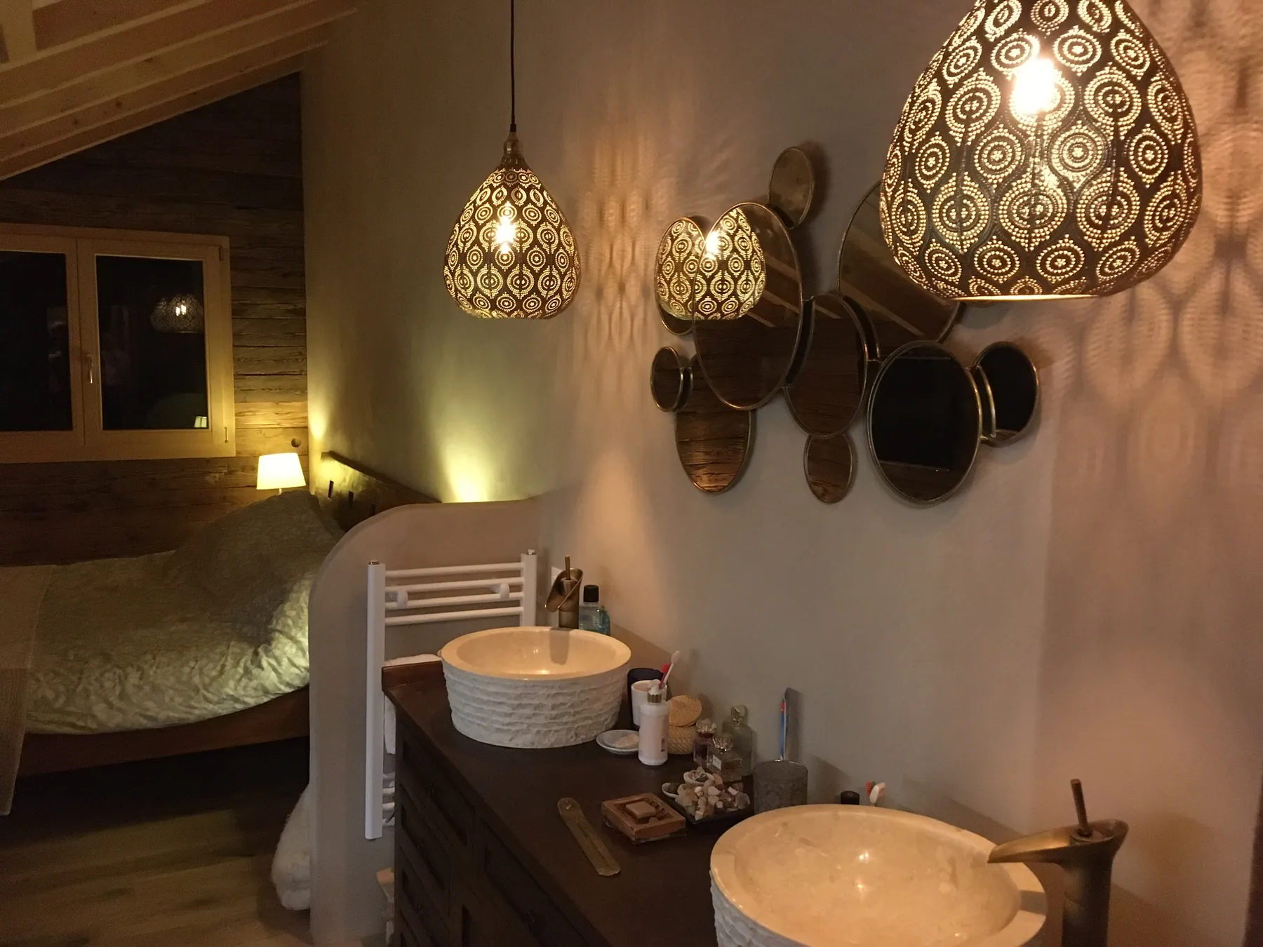 Un meuble de salle de bains avec deux vasques et un ensemble de miroirs ronds décoratifs, illuminé par des suspensions ethniques — chantier Bio Rénovation, Alpes vaudoises