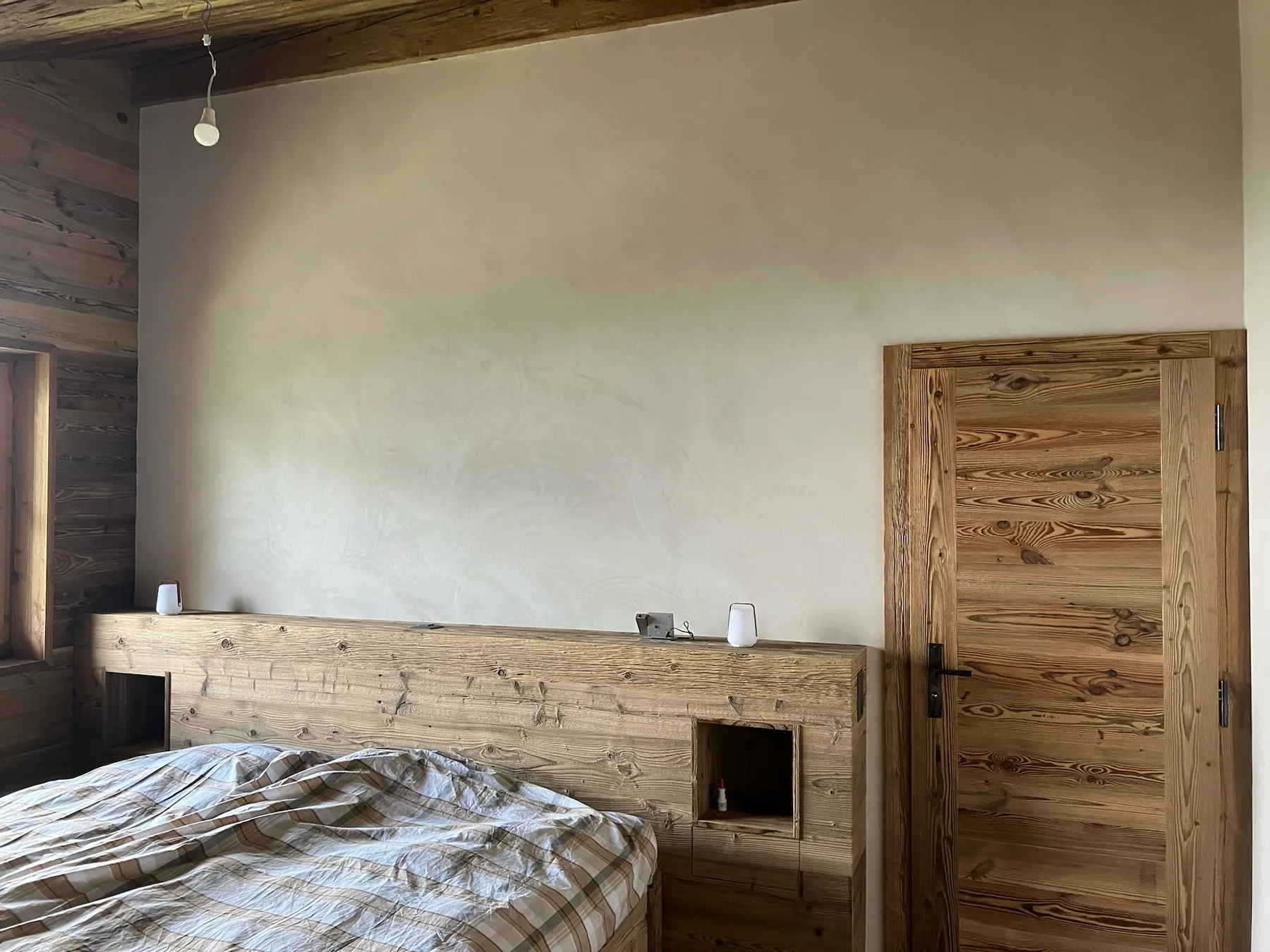 Une chambre avec un grand lit en bois clair intégré, une porte en bois et un mur en enduit clair — chantier Bio Rénovation, Villars-Gryon (VD)