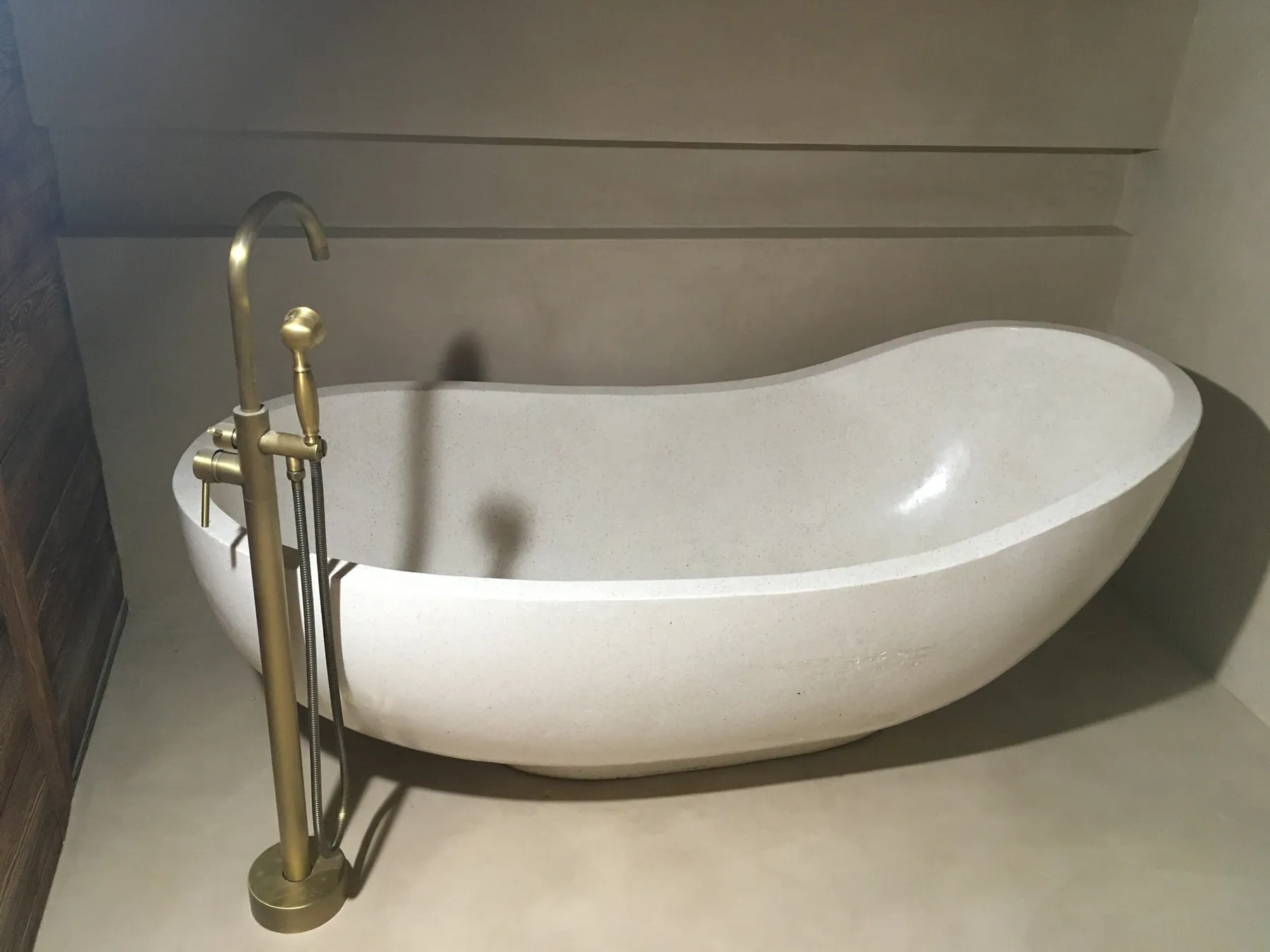 Une baignoire îlot en pierre naturelle ou résine avec un robinet sur pied en laiton brossé, dans une salle de bain aux murs en béton ciré — chantier Bio Rénovation, Riviera vaudoise