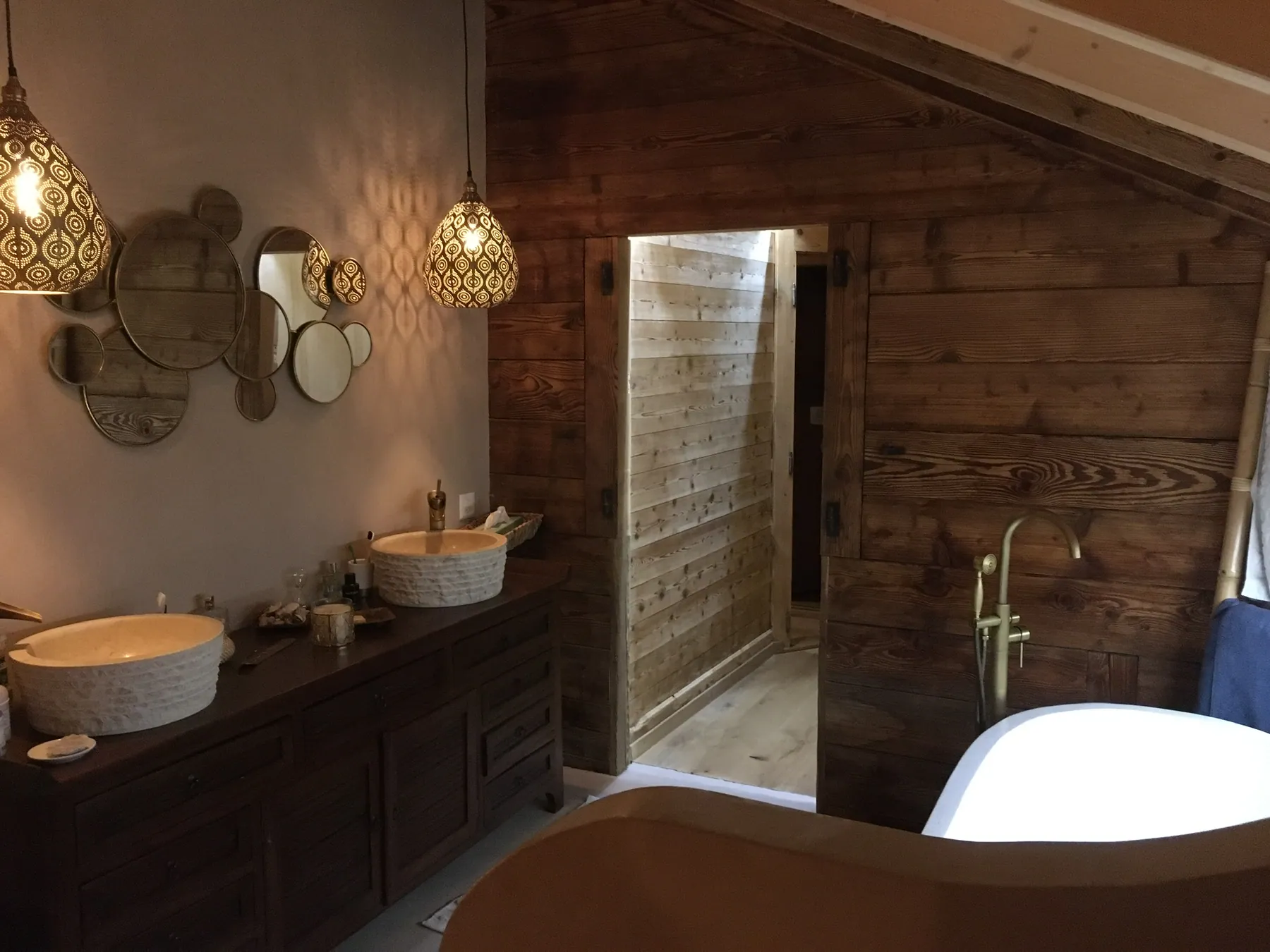 Une salle de bains rustique avec des murs en lambris de bois, deux vasques en céramique sur un meuble en bois foncé et une baignoire blanche — chantier Bio Rénovation, Val de Bagnes / Verbier