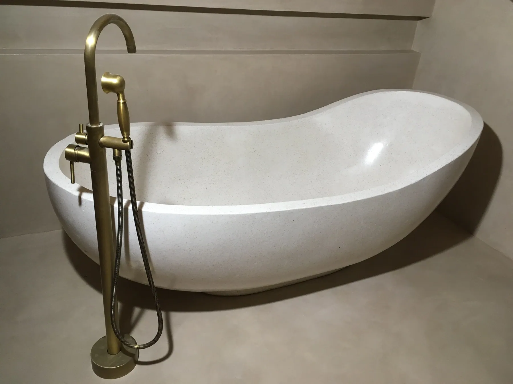 Gros plan sur une baignoire îlot moderne en forme de galet avec un robinet de baignoire autoportant en laiton sur un sol en béton ciré — chantier Bio Rénovation, Riviera vaudoise