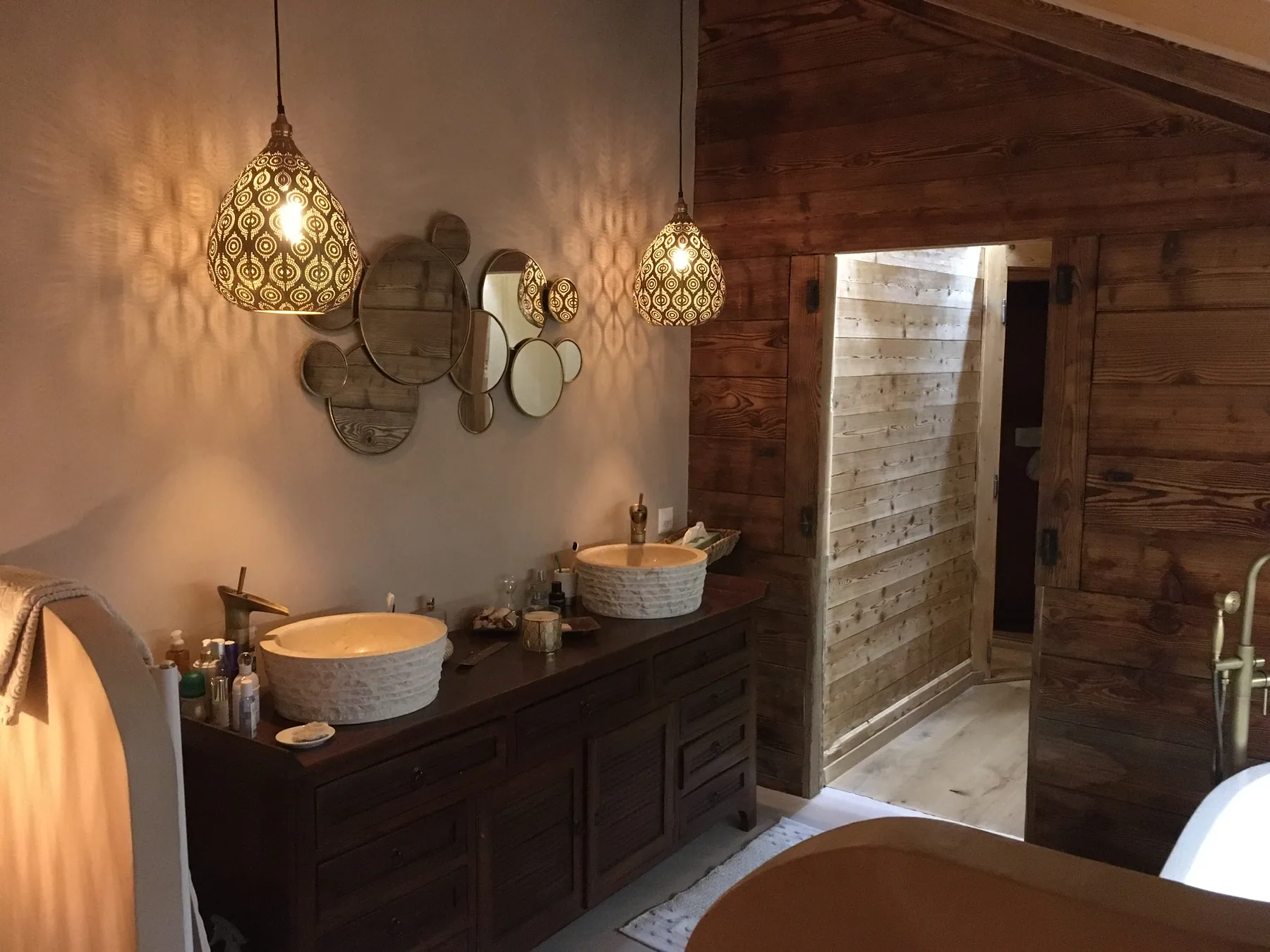 Une salle de bains chaleureuse avec un meuble double vasque en bois, des vasques en céramique et des murs en lambris — chantier Bio Rénovation, Val de Bagnes / Verbier