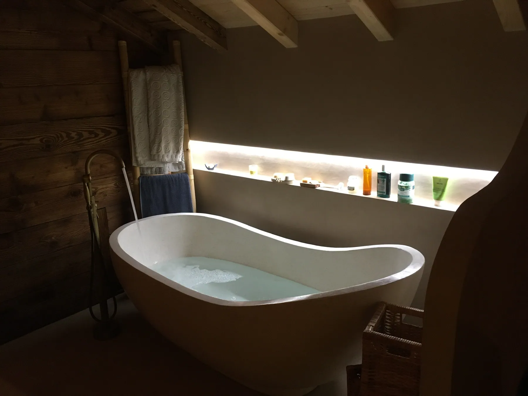 Une salle de bains à l'ambiance chaleureuse avec une baignoire îlot et des murs en béton ciré, éclairée par un bandeau lumineux — chantier Bio Rénovation, Alpes vaudoises