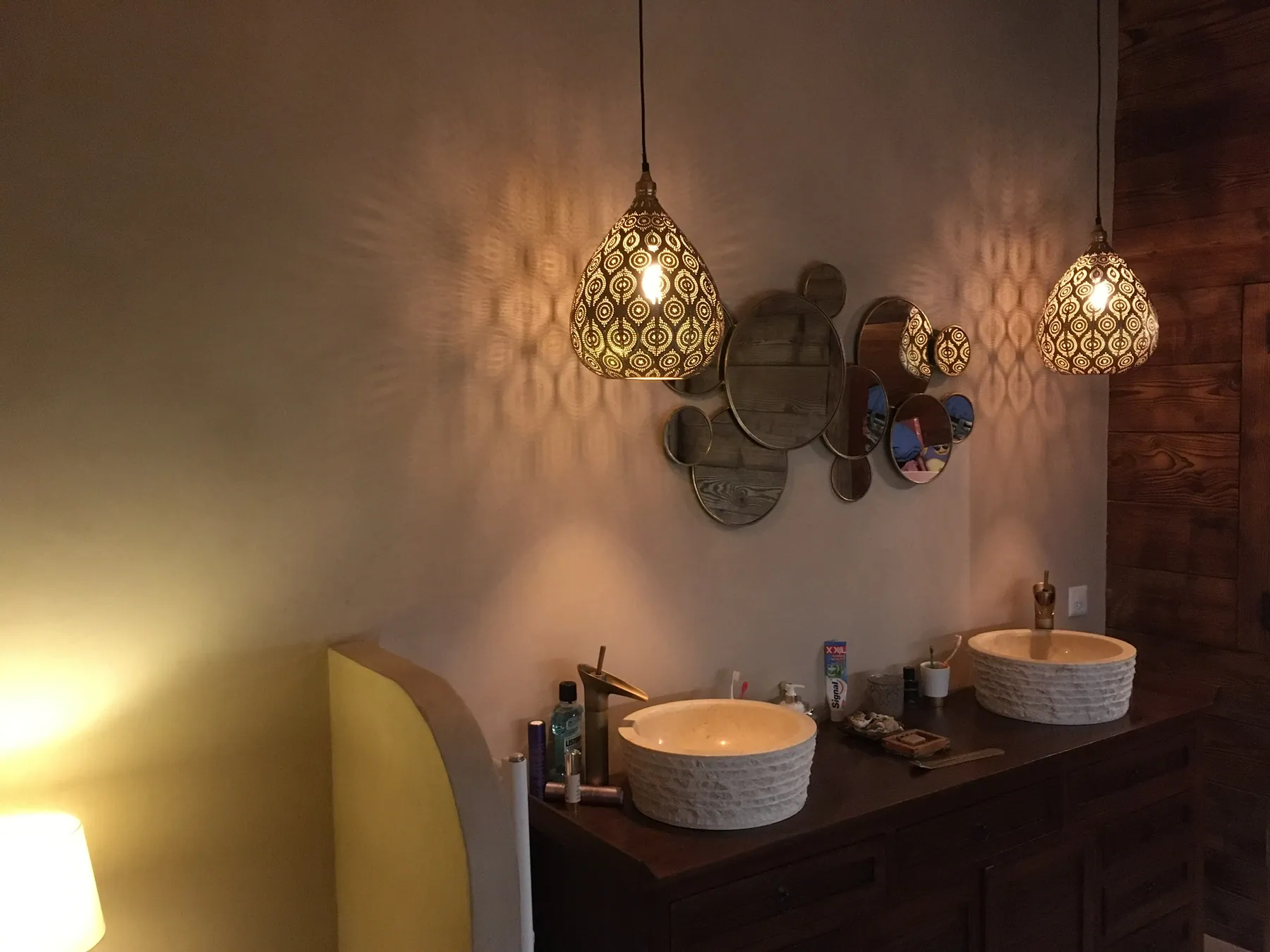 Une salle de bain avec deux vasques en céramique posées sur un meuble en bois foncé, décorée de miroirs ronds et de suspensions lumineuses — chantier Bio Rénovation, Alpes vaudoises