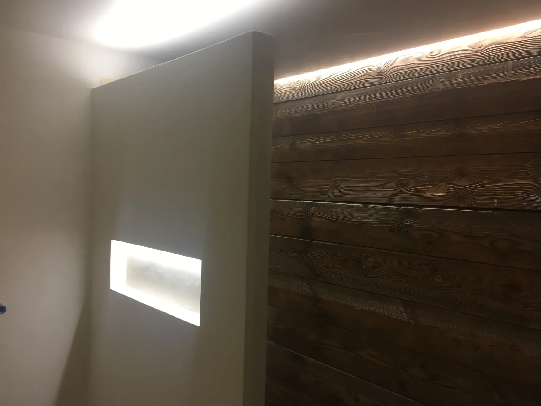Un mur décoratif combinant des tasseaux de bois sombres et un mur clair avec une niche lumineuse intégrée — chantier Bio Rénovation, Chablais