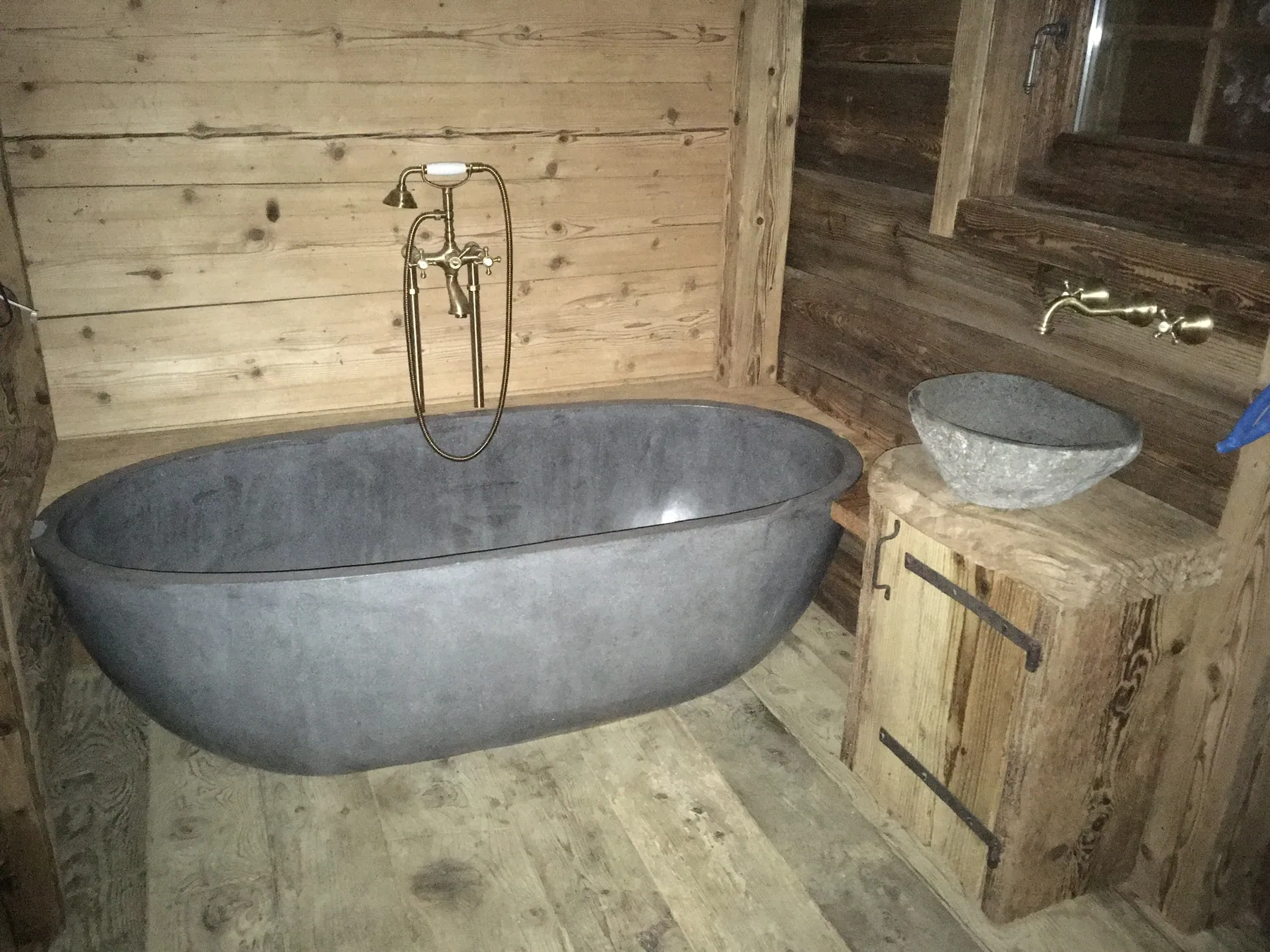 Une salle de bains rustique avec une baignoire autoportante en pierre et des murs et sols en bois — chantier Bio Rénovation, Val de Bagnes / Verbier
