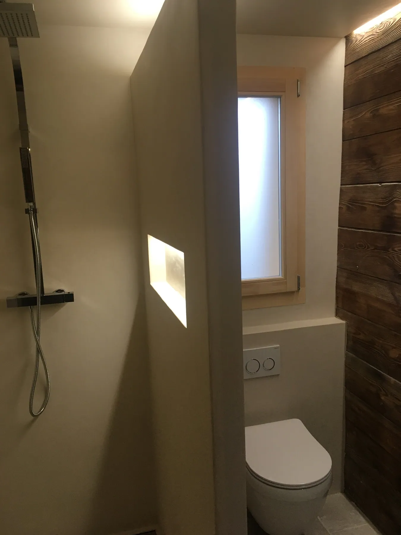 Une salle de bains avec une douche à l'italienne et des toilettes discrètes, combinant murs clairs et revêtement mural en bois — chantier Bio Rénovation, Chablais