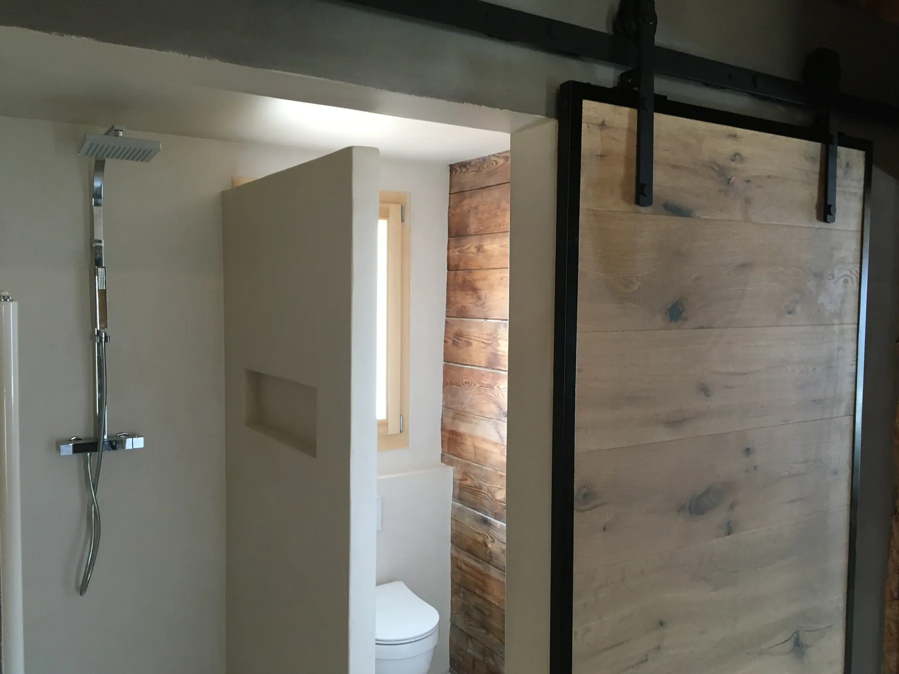 Une salle de bains moderne avec une douche à l'italienne, une porte coulissante en bois clair et un WC séparé avec un mur en bois — chantier Bio Rénovation, Chablais